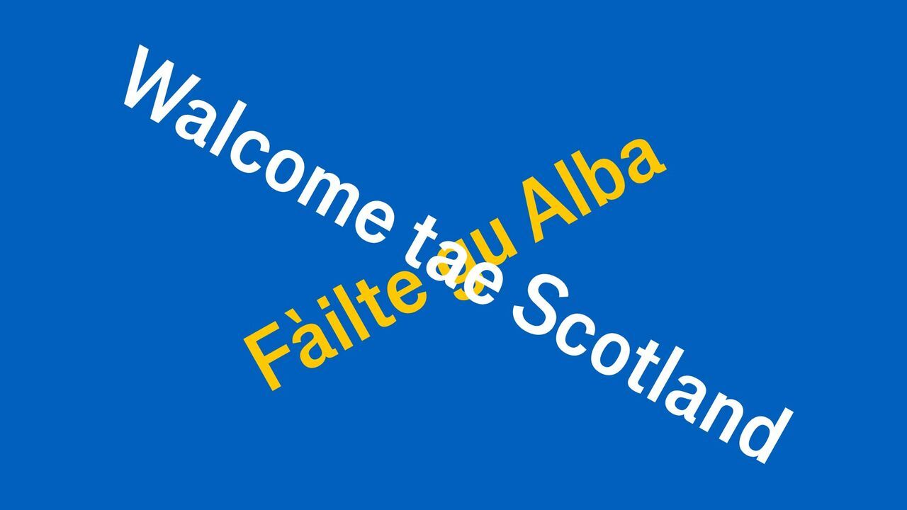 Illustration of the Scottish flag made of words. One sentence is in Gaelic and the other in Scots, saying Welcome to Scotland. 