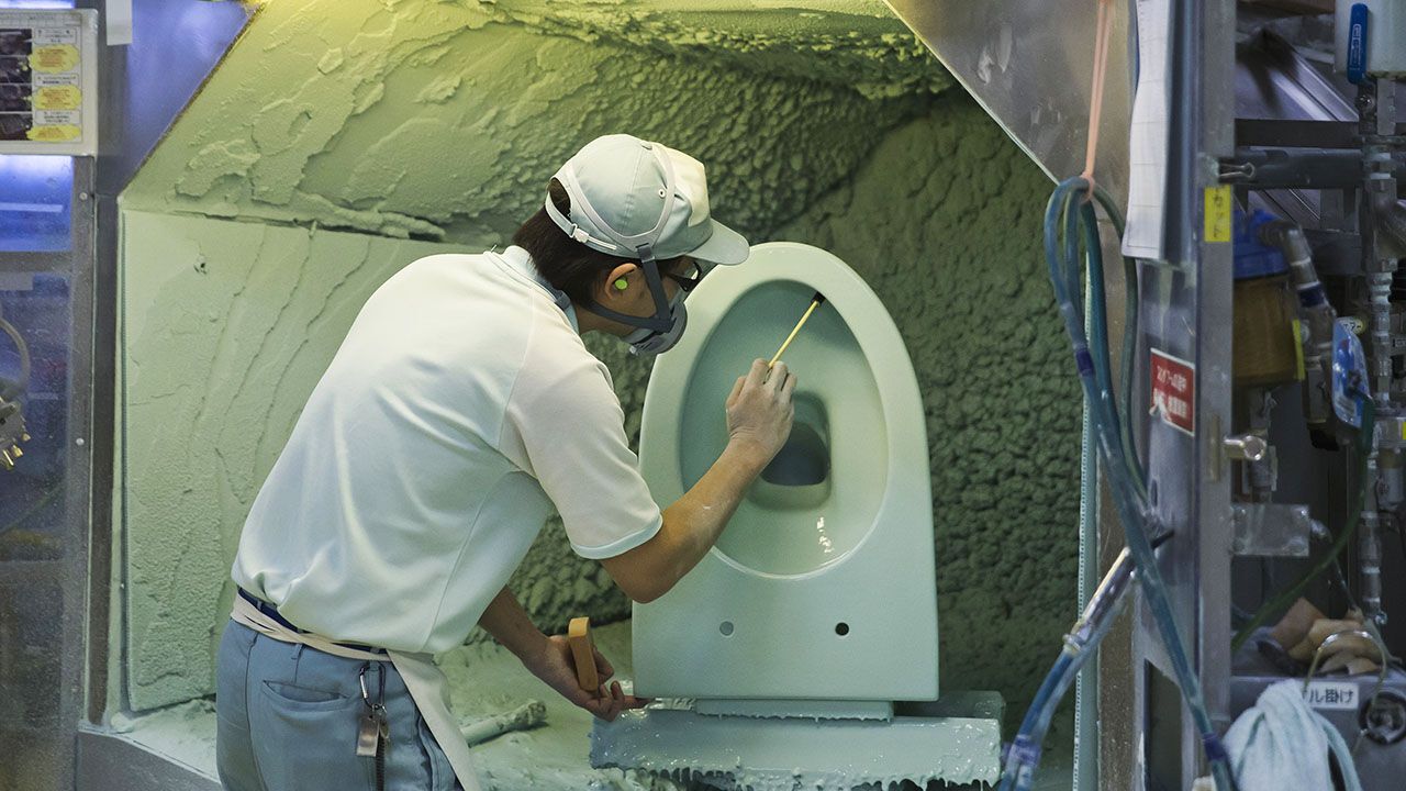 An employee works on a toilet bowl in the painting section of the Toto Ltd. factory in Kitakyushu, Fukuoka, Japan