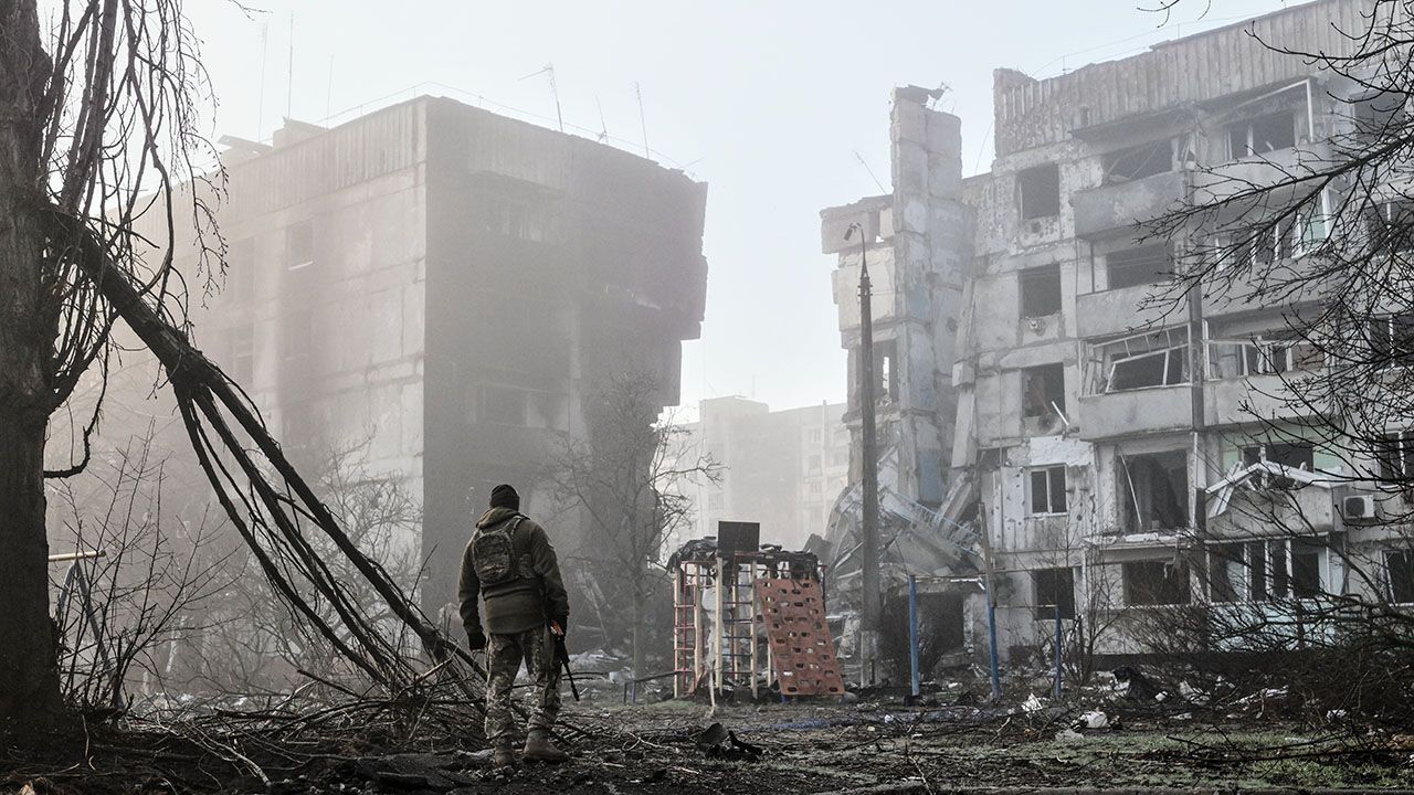 A lone soldier stands in front of apartment buildings damaged in Ukraine.