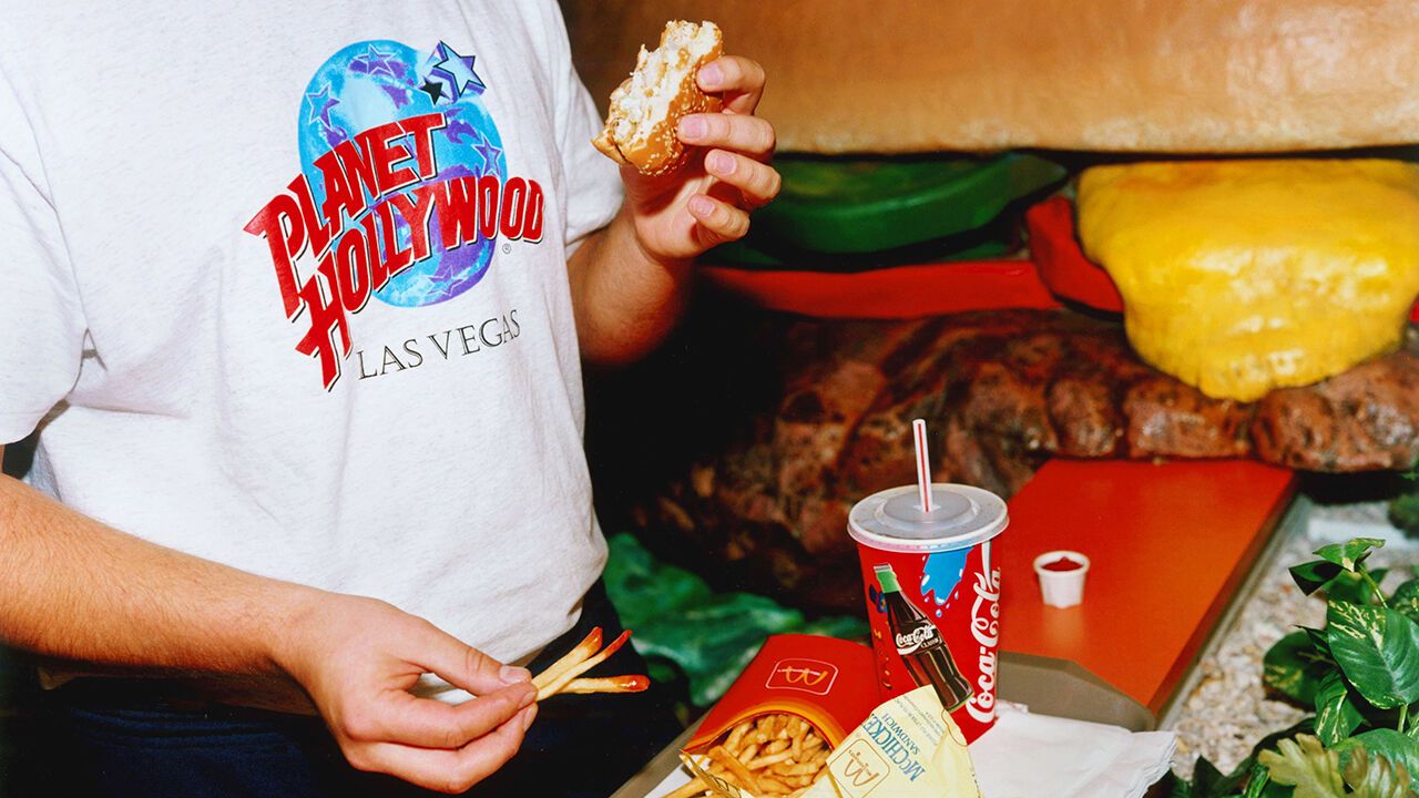 A customer wearing a Planet Hollywood t-shirt eats McDonalds.
