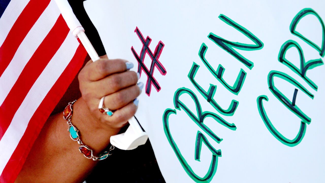 A demonstrator holds a small American flag and sign reading 'green card'.