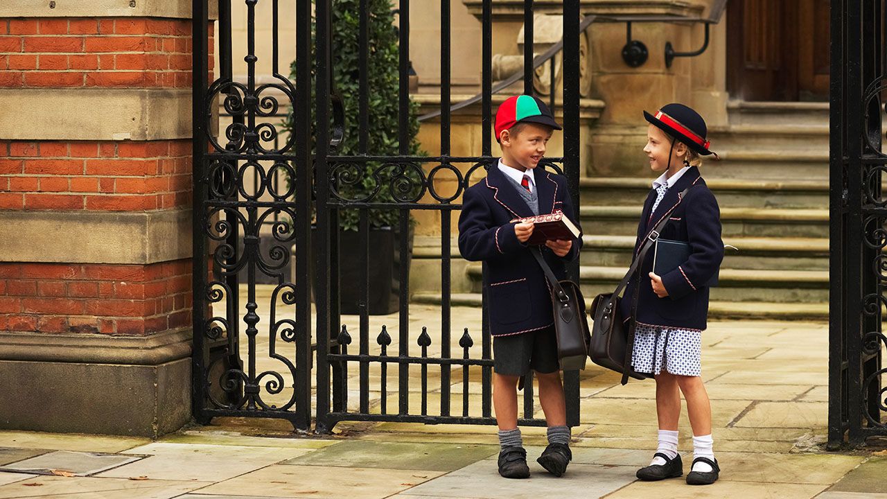 Young boy and girl students in uniform talk outside their school