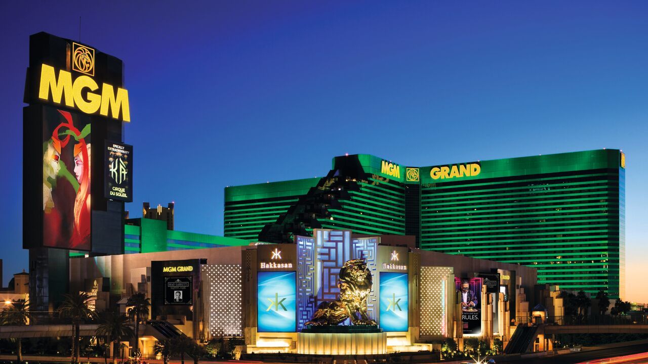 Exterior of the MGM Grand Las Vegas shows a green, glass, L-shaped building with 29 floors with the casino and gold statue of the MGM lion in front.