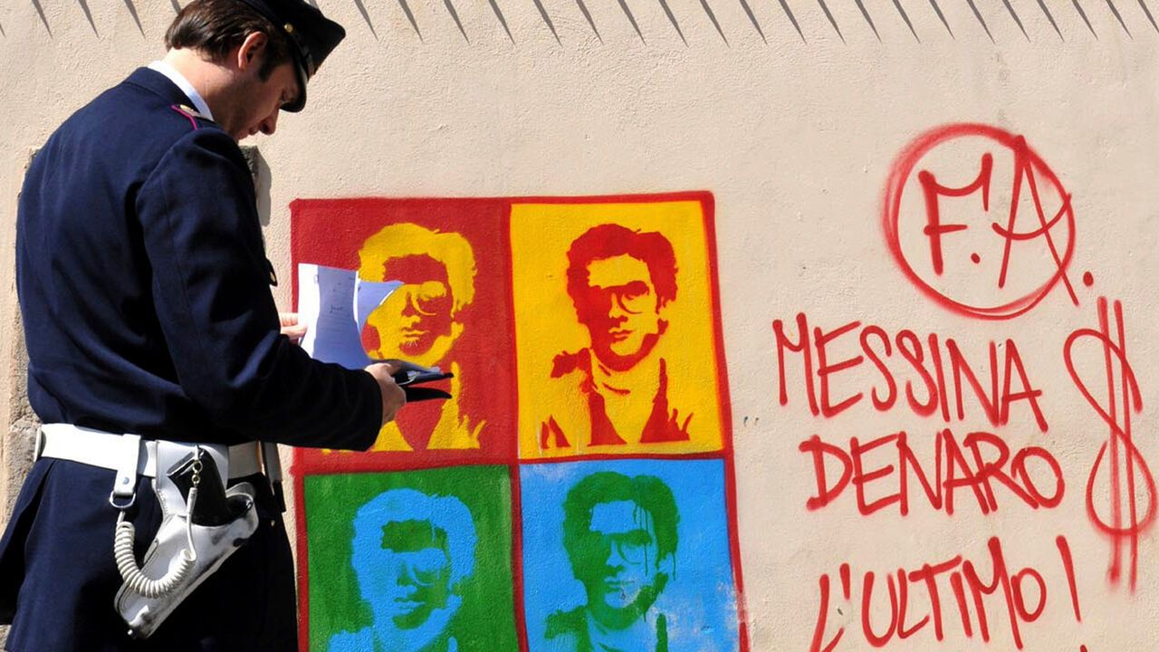 An Italian Police officer looks on at graffiti on the perimeter wall of Palermo's city's cathedral, portraying Matteo Messina Denaro, in Sicily, southern Italy