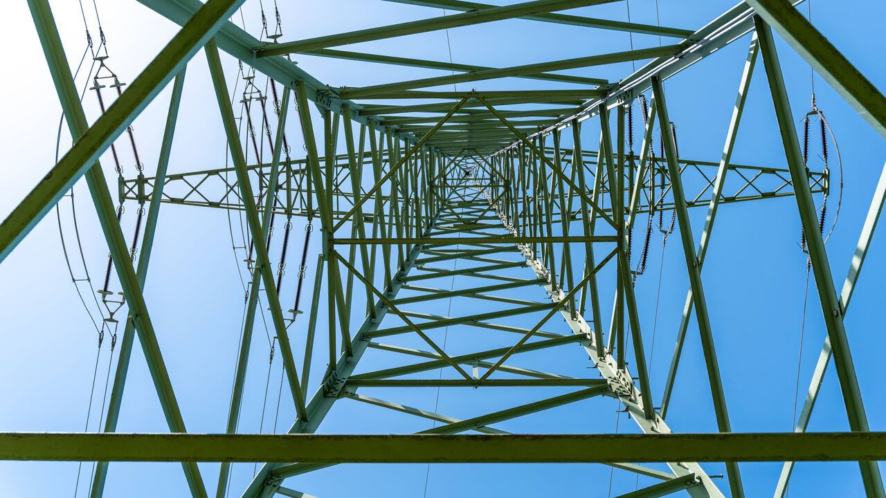 An upwards view of a high-voltage power pylon with power lines against a blue sky in Bavaria, Germany.