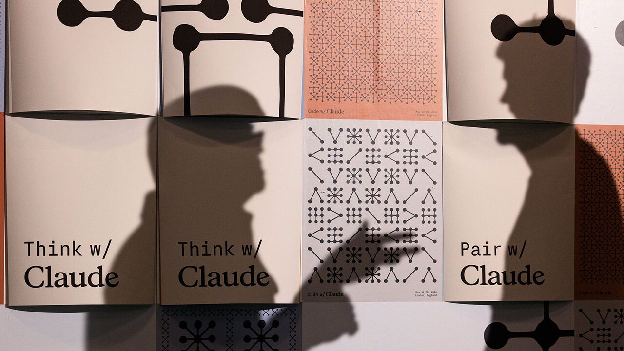 A person is silouhetted agaist Claude Code posters at a developer conference in London