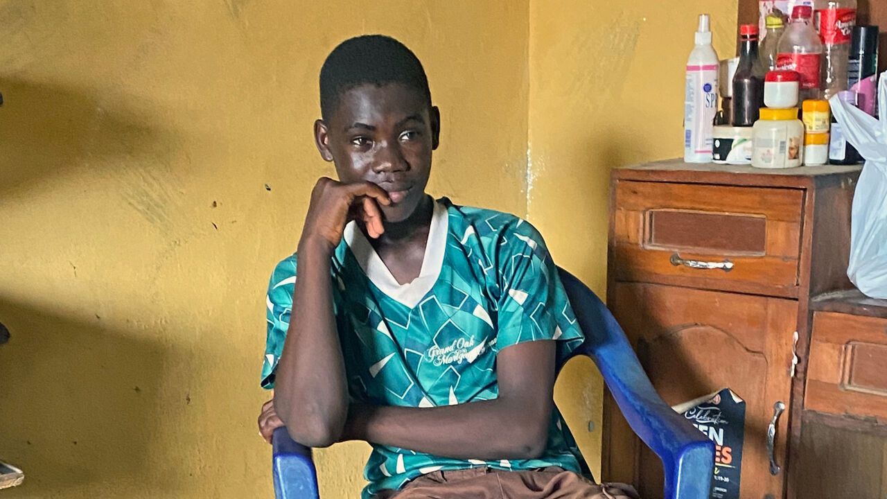 A small boy who had previously worked as a scammer sits in a chair in Ikotun, Nigeria.