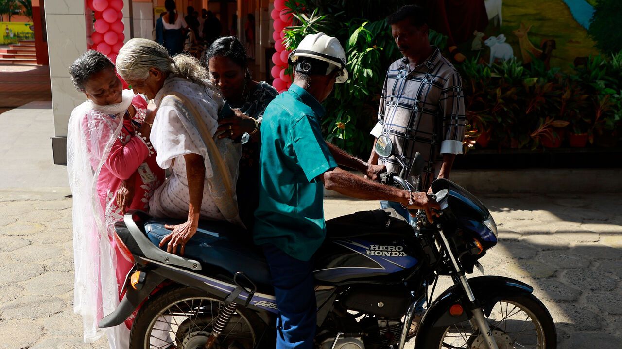 Election officials assist an elderly woman onto a motorcycle after she casts her vote at a polling station during the Kerala state assembly election in Kochi, India.