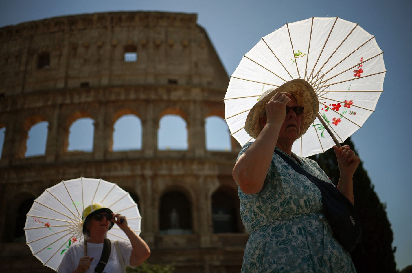 Tourists use umbrellas to shelter from the sun near the Colosseum