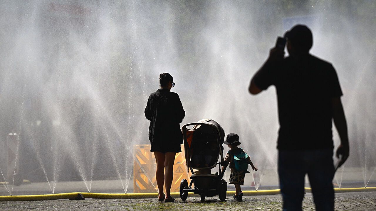 People stand near over water hoses spilling water to provide relief from the summer heat as part of Cologne's climate adaptation measures in Cologne.