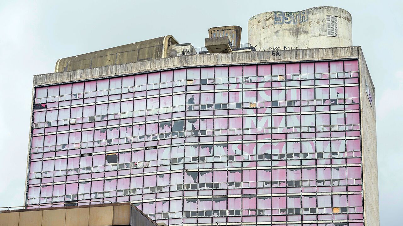 The decayed "Glasgow" sign on a tower block of the former Glasgow College of Printing, with people and buildings at the city of Glasgow, Scotland