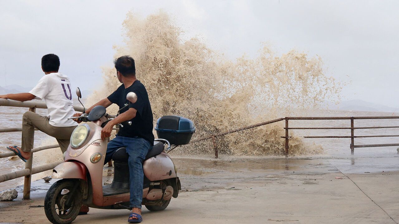 People look on as large waves crash against the coast from Typhoon Bavi in China