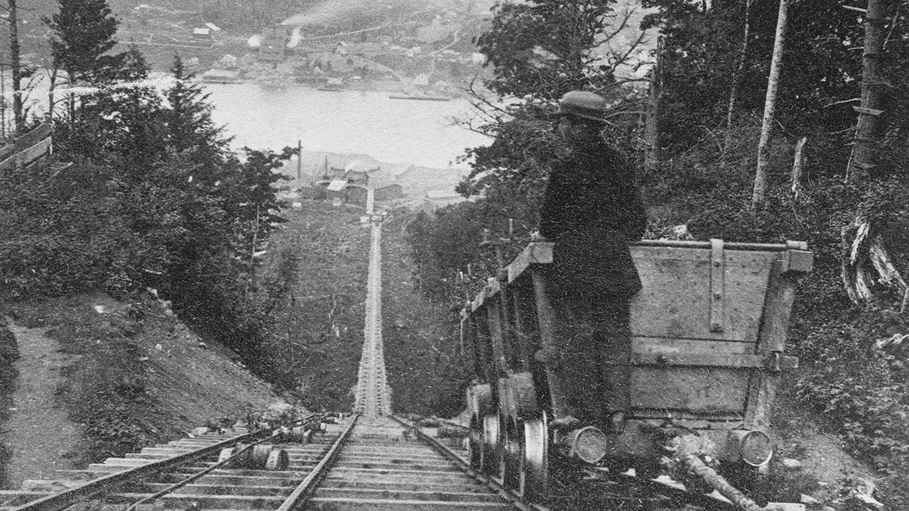 Stereoscopic image of a man standing on the back of a minecart on the Franklin tram road, which extends down the hill, in the copper mines of Lake Superior, Michigan, circa 1875.