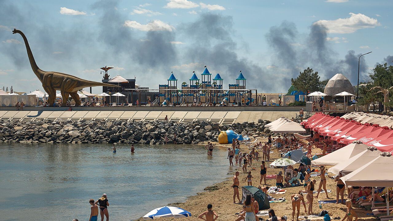 Local residents and visitors relax on a beach on the outskirts of Odesa as smoke from a fire rises in the background following a Russian missile strike on July 29th.