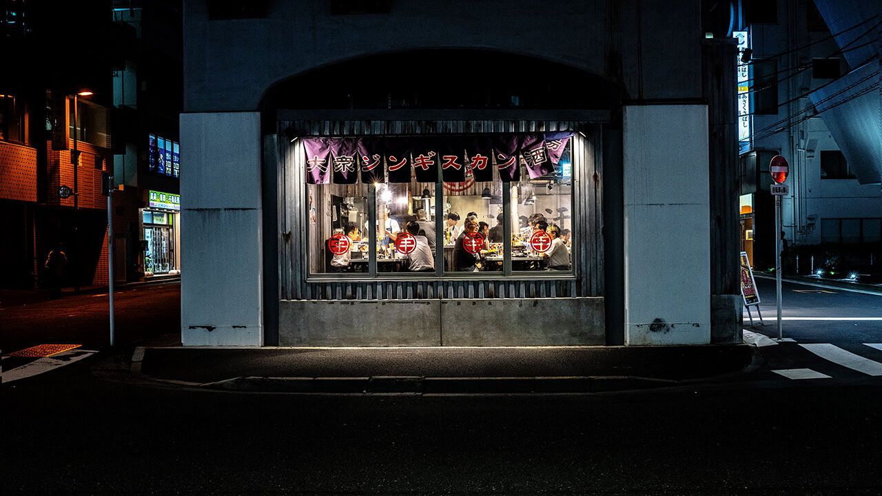 Diners eat inside a in barbecue restaurant in Tokyo's Asakusabashi district, Tokyo - pictured at night, the glow of the restaurant can be seen from the dark street.
