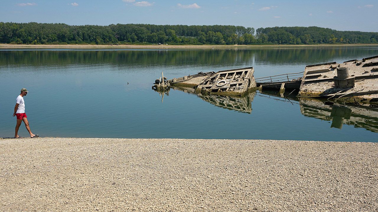A man walks on the sandbank by the wreckage of a WWII German warship on the River Danube