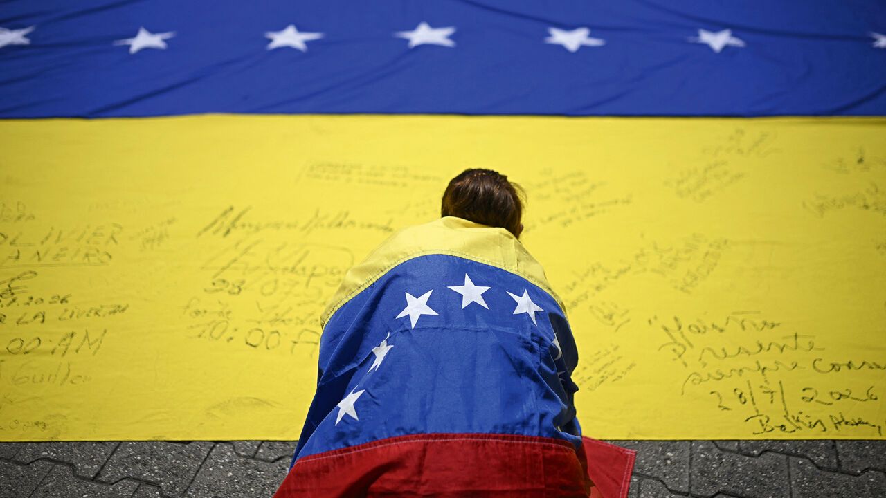 A unionist wrapped in a Venezuelan national flag, signs another Venezuelan national flag during a protest march in demand of elections in Caracas.