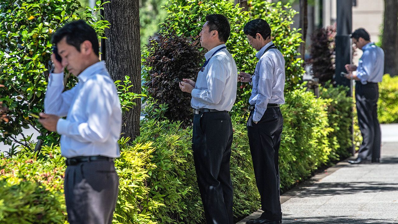 Japanese salarymen check their phones as they stand along a street in the Marunouchi financial district in Tokyo, Japan.
