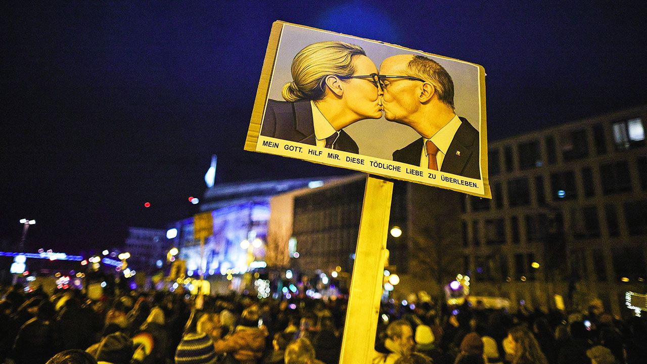 A demonstrator holds a banner with an AI image depicting Alice Weidel kissing Friedrich Merz