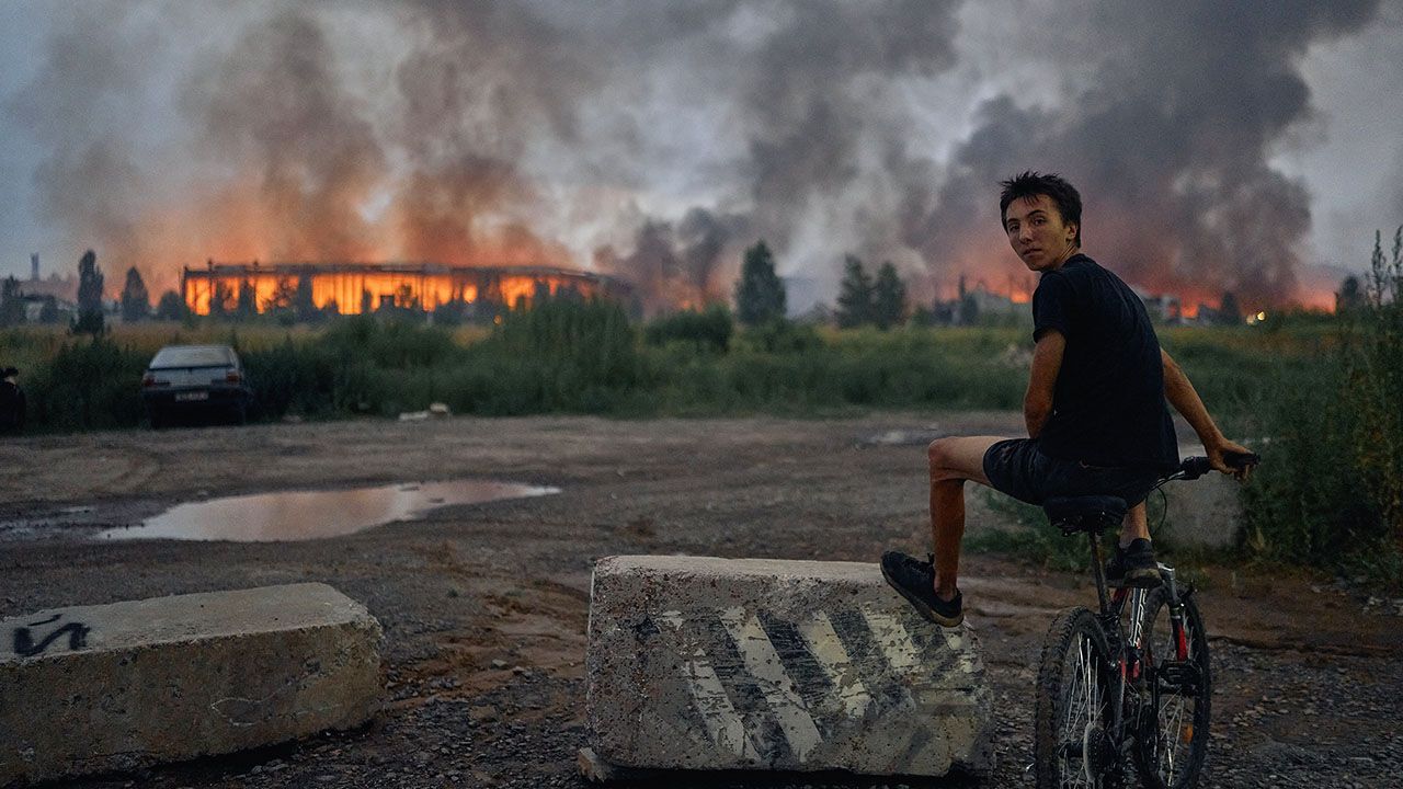 A teenager sits on a bicycle watching flames rise from a burning logistics warehouse following a Russian ballistic missile attack on Kyiv