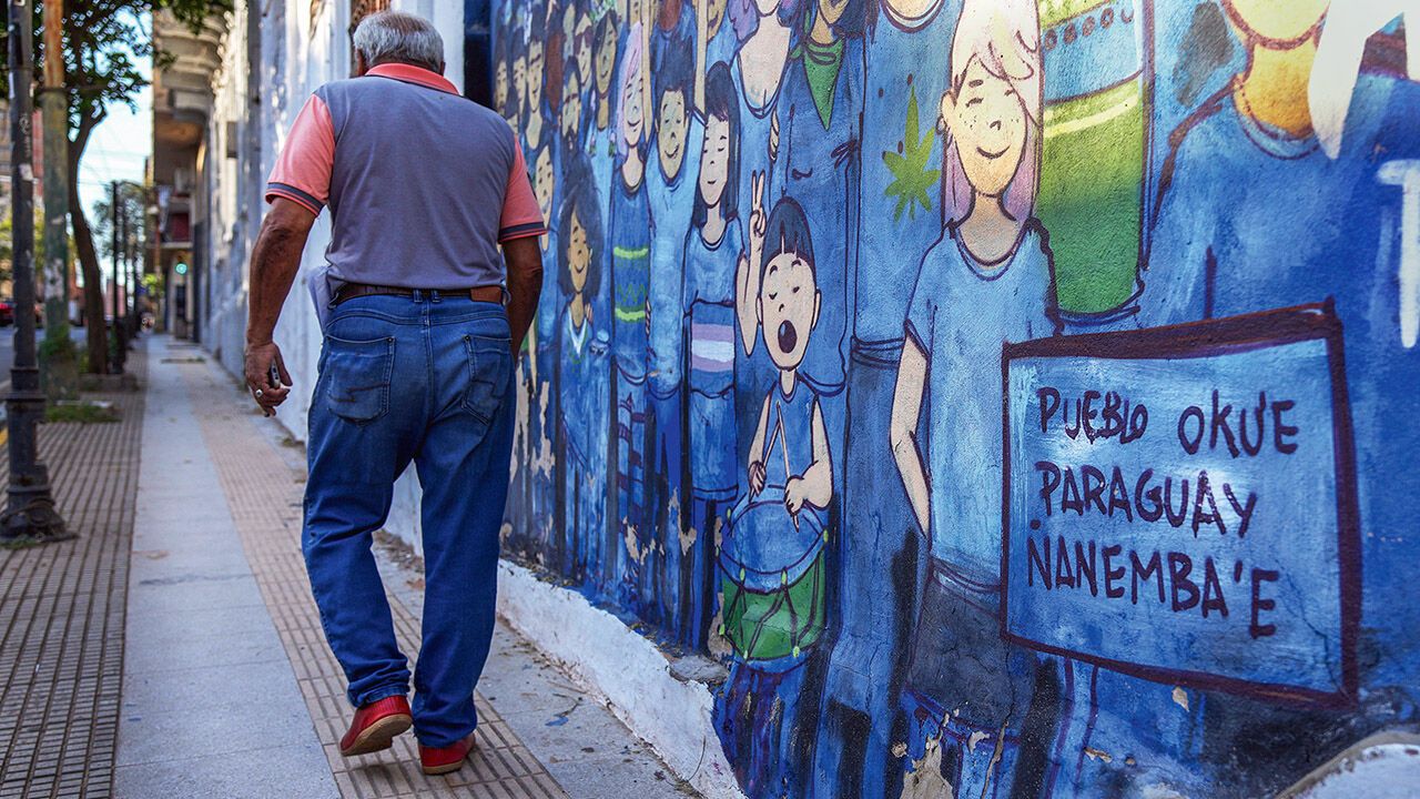 A pedestrian walks past a mural that says in the Guarani language "Ñanemba'e okue, are ko pueblo" which means "The people are on the move, ours"