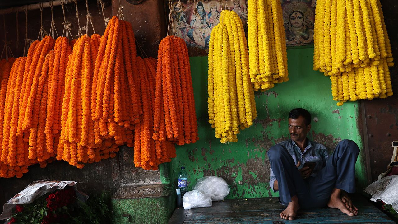 A flower vendor with marigold garlands waits for customers at a wholesale flower market in Kolkata, India, on August 21, 2026.