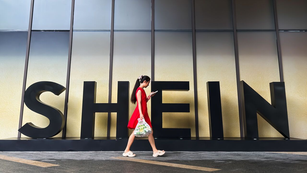A woman looks at her smartphone while walking past a SHEIN sign outside the company's office on July 14, 2026, in Guangzhou, Guangdong Province, China