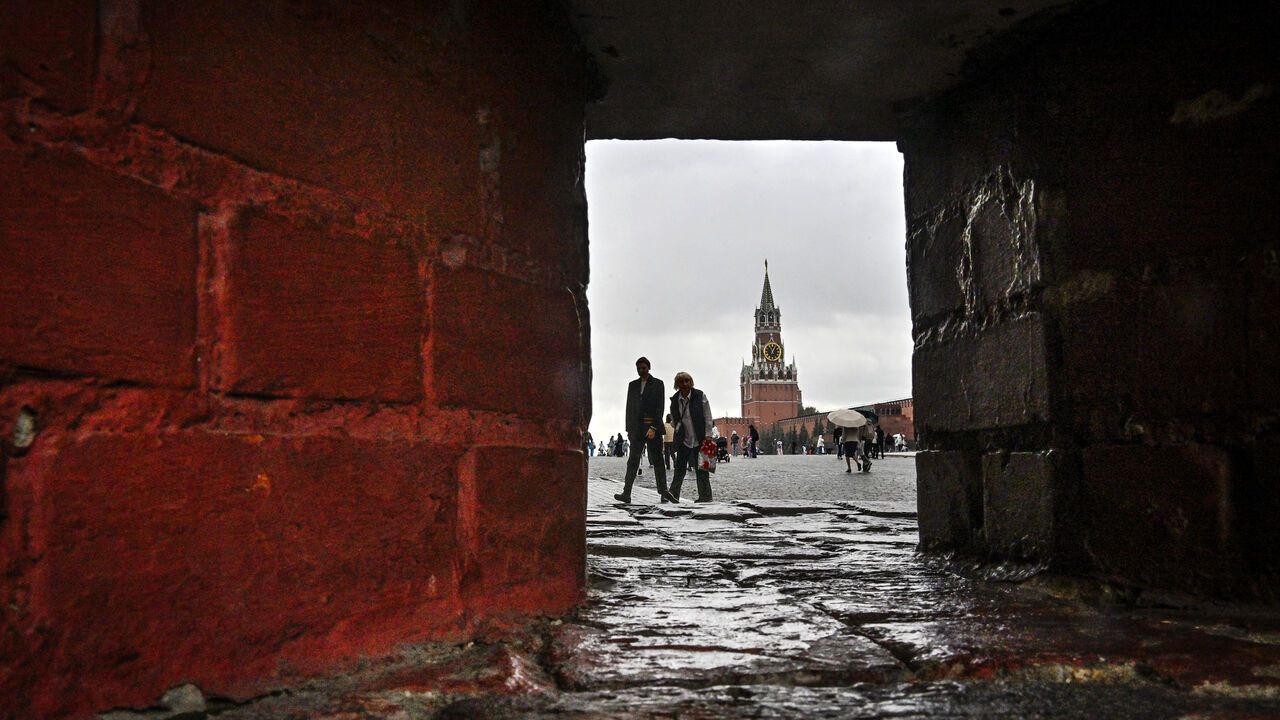 A view through a narrow brick doorway with people walking in front of the Spasskaya tower at Red Square in central Moscow, Russia.