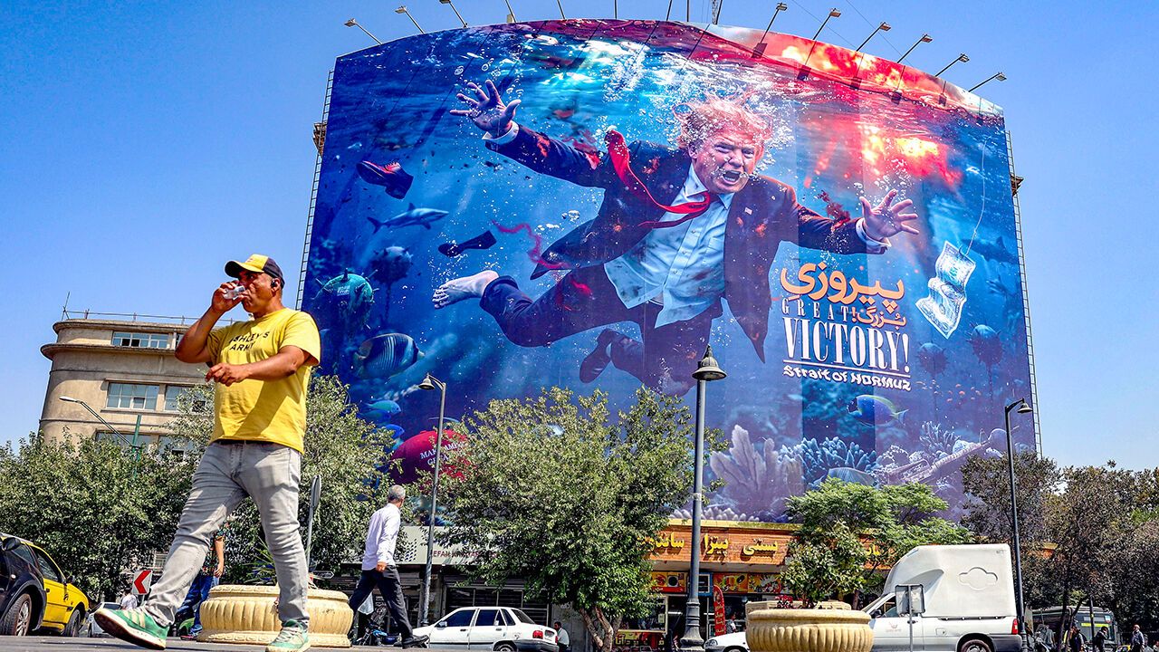 Iranians walk past an anti-US billboard featuring US President Donald Trump in southern Tehran, Iran.
