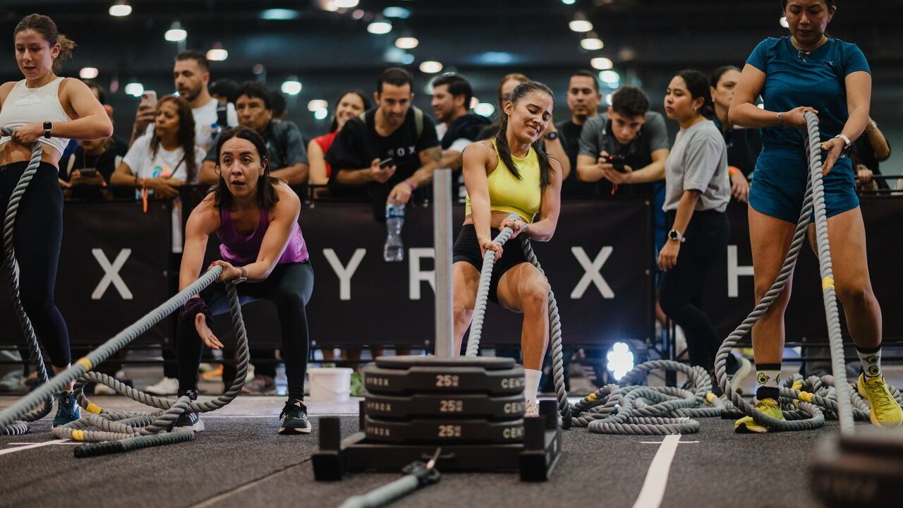 Women pull weighted sledges at a Hyrox competition.