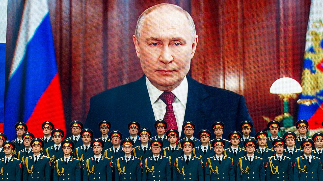 Vladimir Putin's face on a large screen above rows of uniformed military officers.