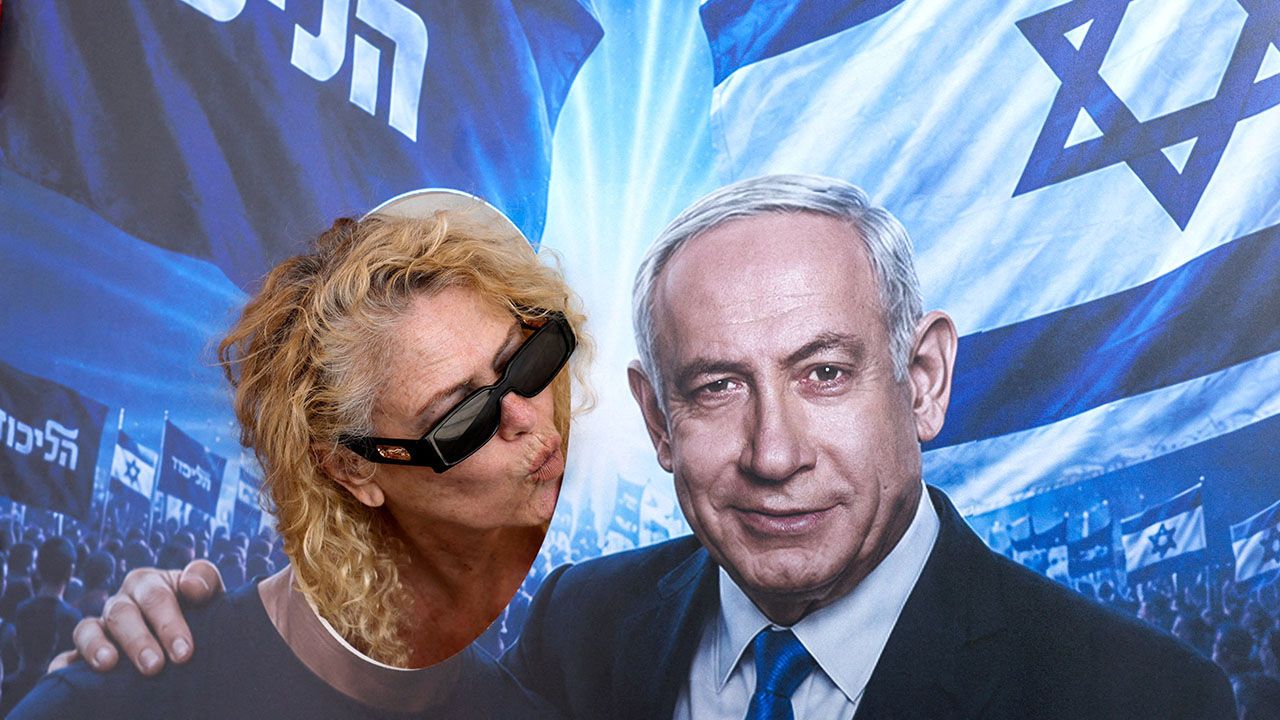 A woman poses in a face-in-the-hole picture cutout, blowing a kiss towards a depiction of Israeli Prime Minister Benjamin Netanyahu