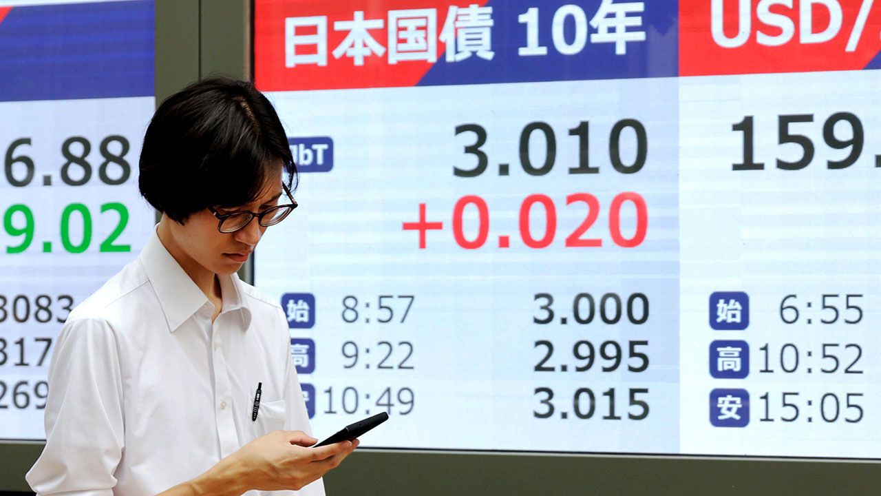 A passerby walks walks past a screen (C) showing the yied on the 10-year Japanese government bond in Tokyo, Japan