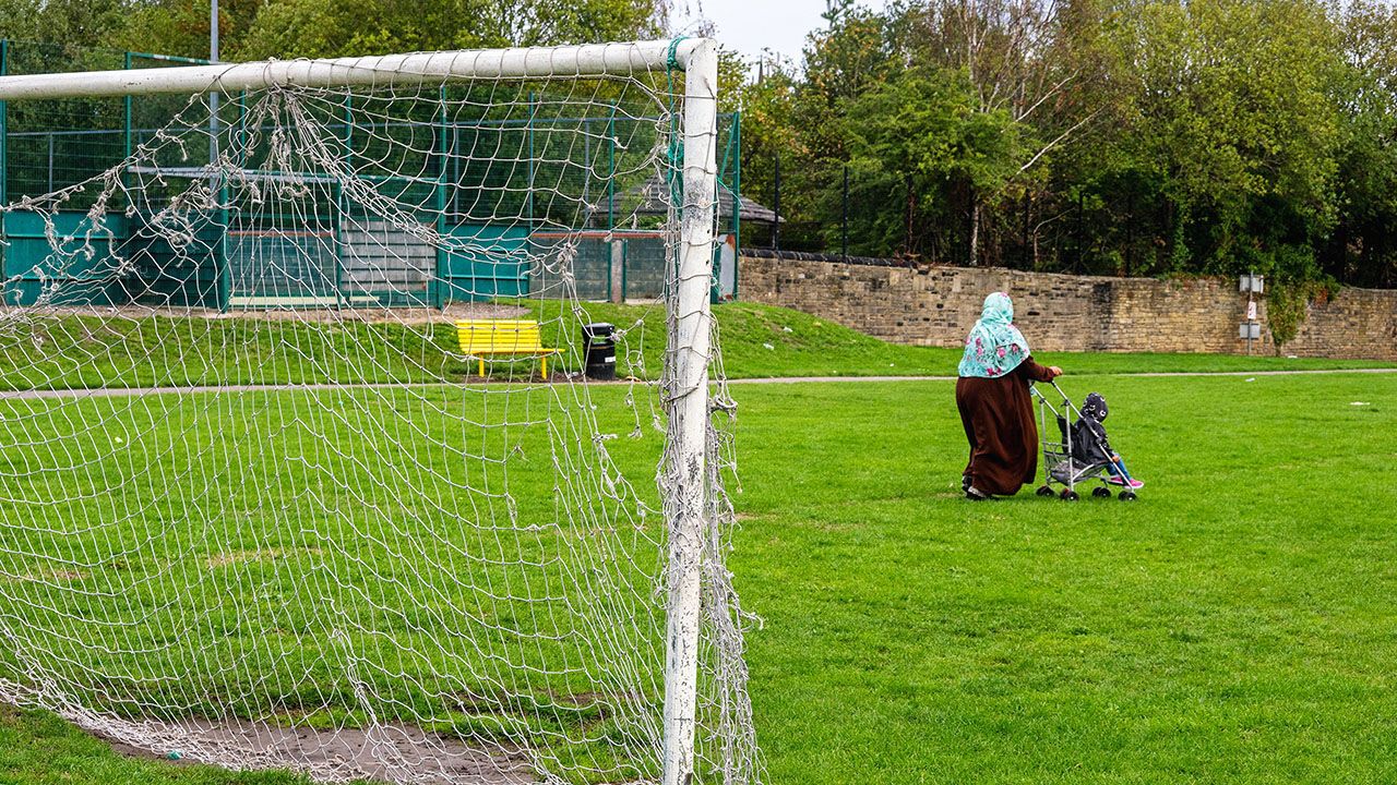 A woman and child walk through a play area towards Drummond Road.
