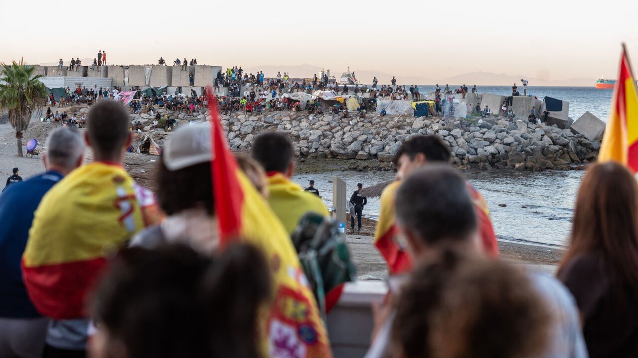 Demonstrators against the presence of migrants look at migrants camping on the Trampolin beach in Ceuta, Spain.