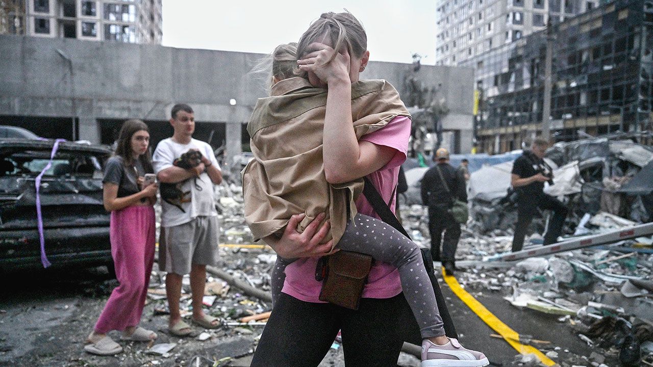 A woman holds her child outside damaged residential buildings in Kyiv