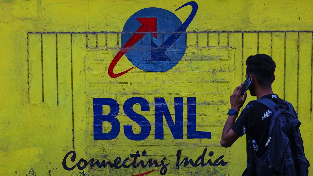 A man is talking on his mobile phone past the logo of Bharat Sanchar Nigam Limited (BSNL) in Srinagar, Jammu and Kashmir