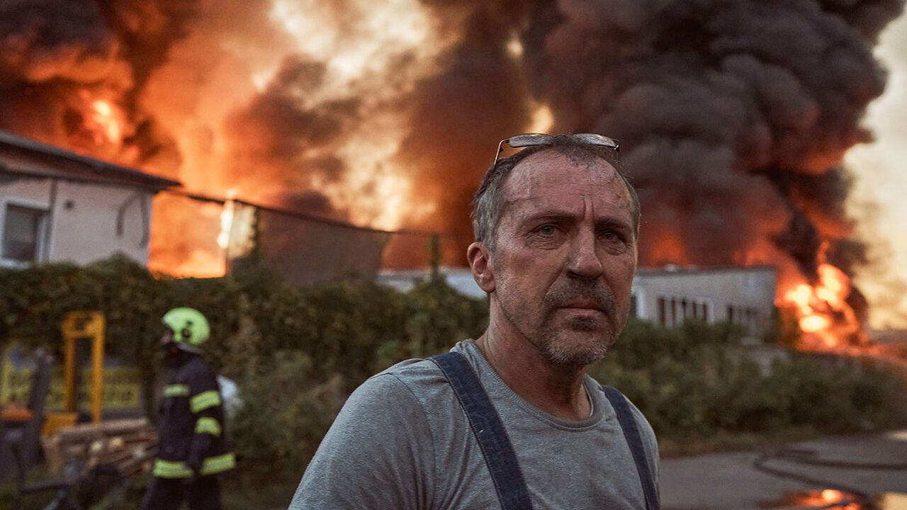 A man looks on as members of emergency services work to contain a fire in the aftermath of a Russian missile and drone attack in Kyiv