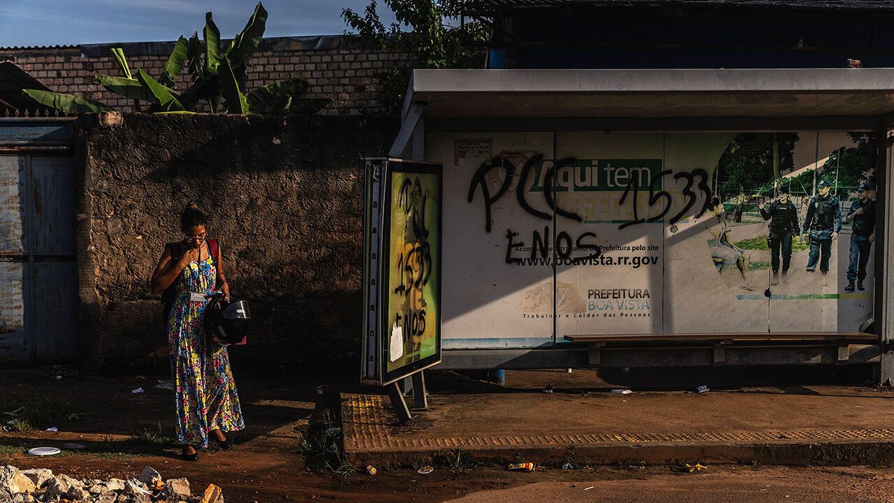 A resident waits on a bus station marked with graffiti from PCC criminal group, Brazil.