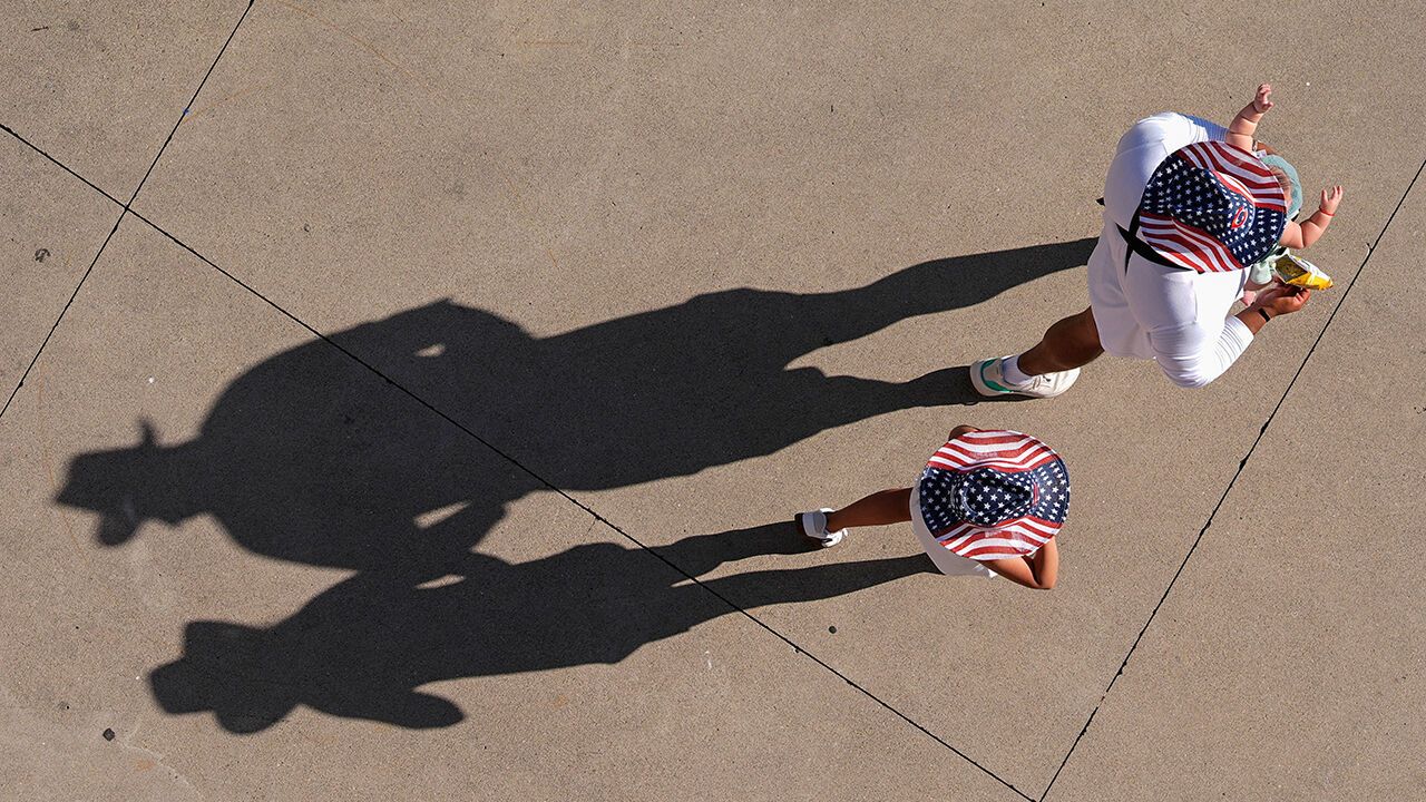 Fans with red, white and blue cowboy hats and a baby walk along the concourse