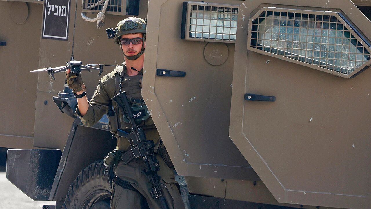 An Israeli soldier carrying a small drone exits a vehicle.