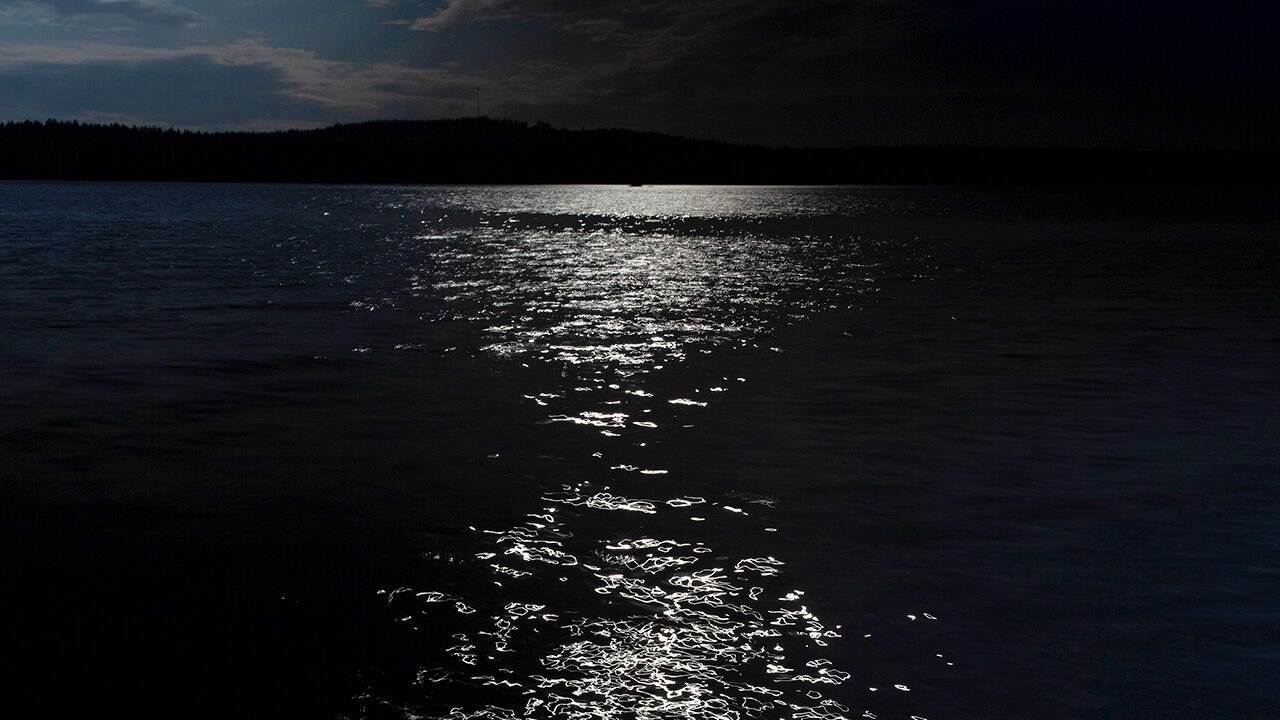 Reflections of moonlight ripple across the surface of a lake under a dark evening sky.