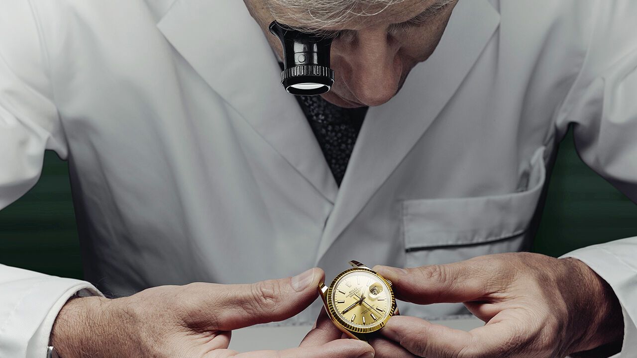 A watchmaker looks at the inside of a Rolex watch through a magnifying glass