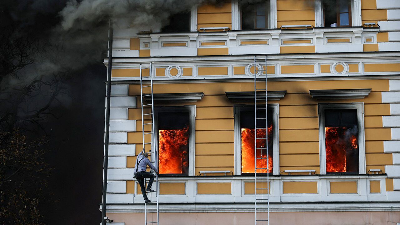 A man climbs down a ladder as flames rise from an administrative building hit by a Russian jet-powered drone strike, in Kyiv, Ukraine