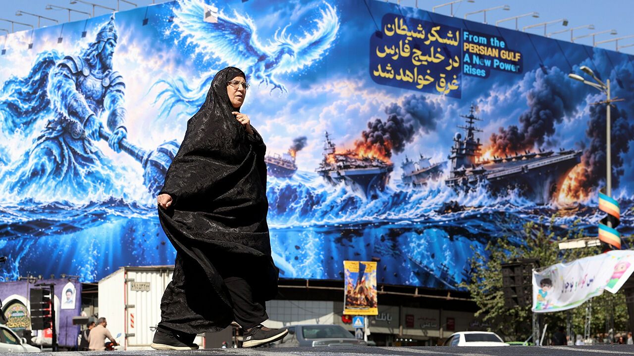 A veiled woman walks past a propaganda poster in Tehran