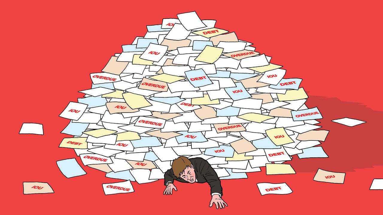 A figure representing the government is buried beneath a pile of bills and debt papers.