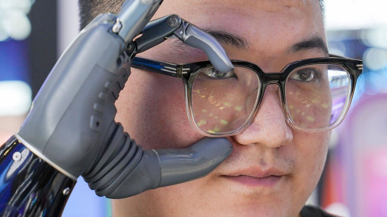 A staff member of technology firm BrainCo uses a smart prosthetic hand to take off his glasses in the Digital Technology Chain exhibition area at the third China International Supply Chain Expo in Beijing