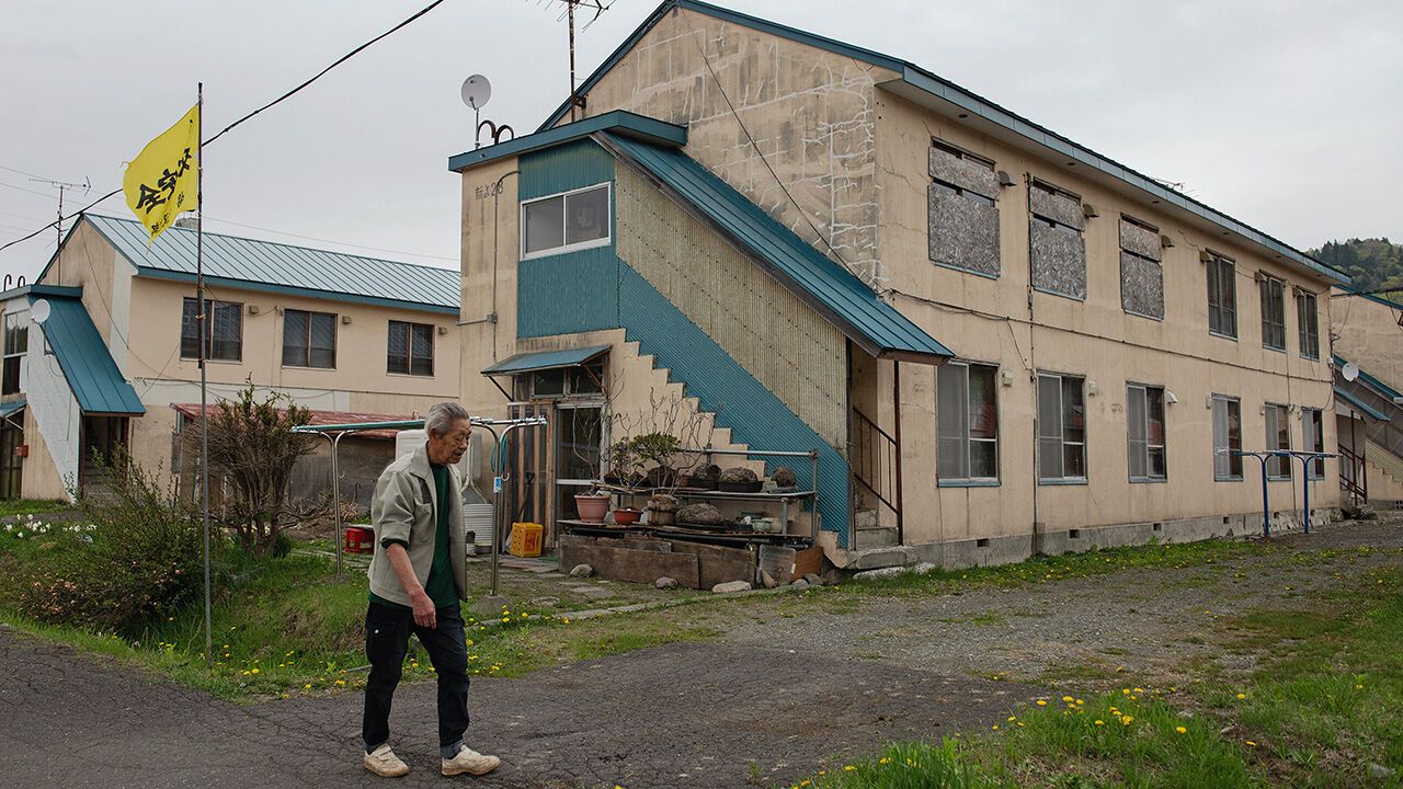 An elderly man walks in front of an apartment buildings where many of the residences are boarded up and empty in Yubari Japan, on May 2022.
