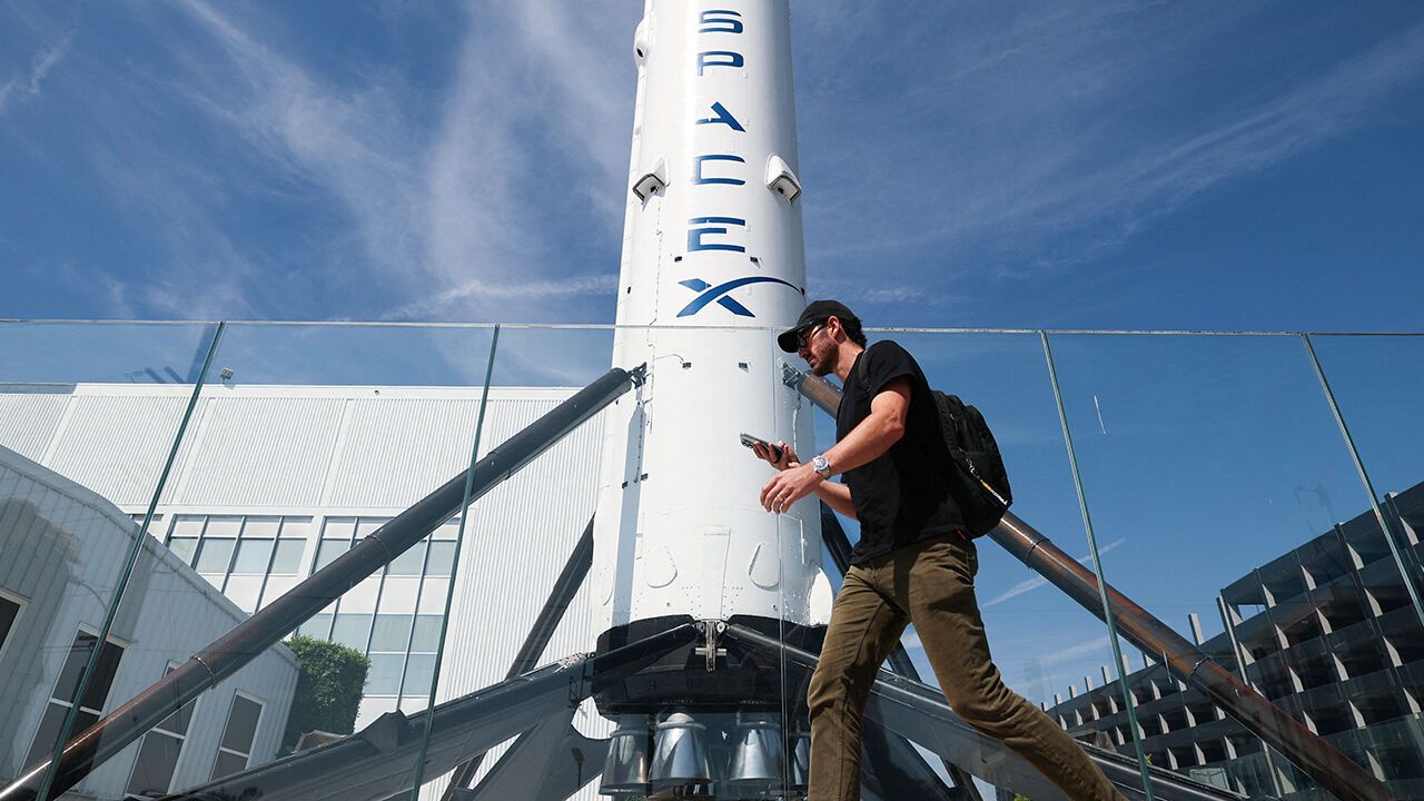 A man, using a smartphone, walks past a SpaceX Falcon 9 rocket at the Space Exploration Technologies Corp. facility in Hawthorne, California
