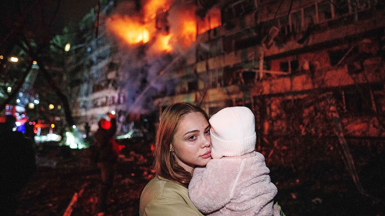 A woman holds her daughter while standing in front of a multi-story residential building damaged in a Russian missile strike in Kyiv, Ukraine.
